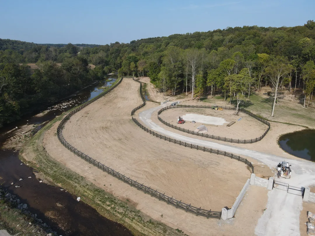 Aerial view of a graded riding arena and track shaped along a creek