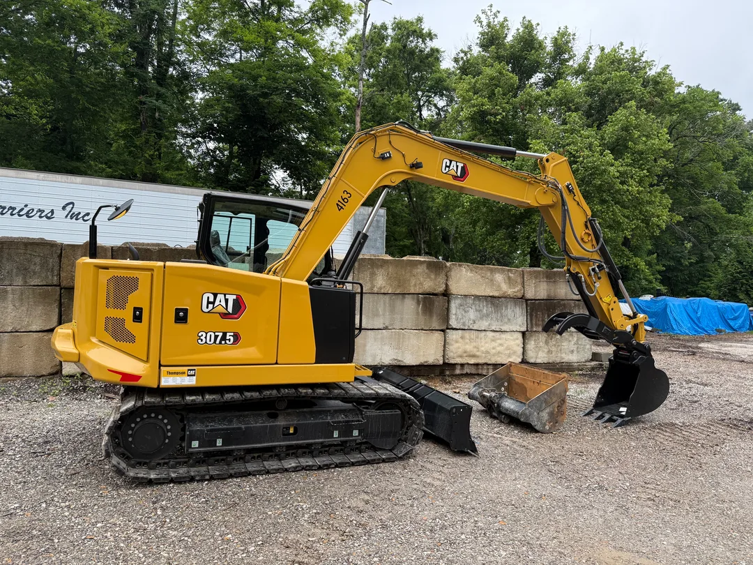 Compact excavator working beside a block wall on a gravel base