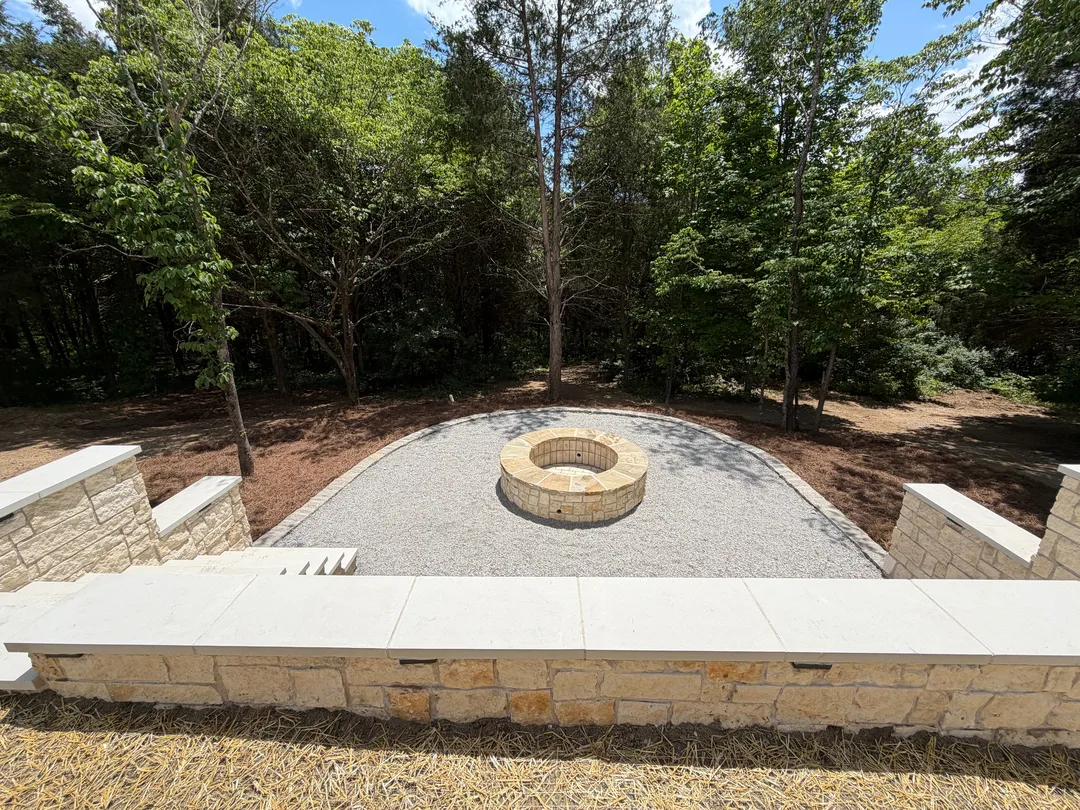Stone fire pit and seating wall overlooking a green lawn